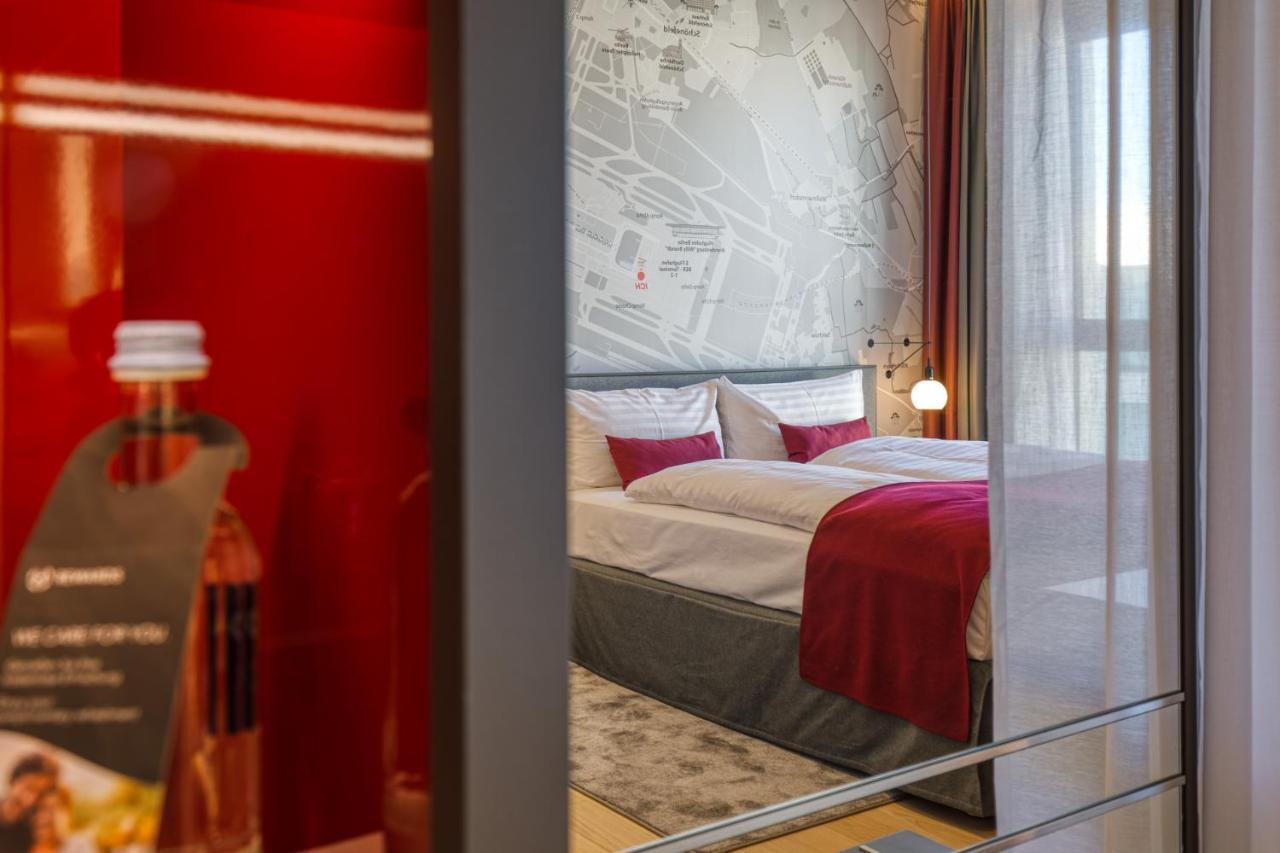 Intercityhotel Berlin Airport Ber Terminal 1 & 2 Schönefeld Extérieur photo The photo shows a modern hotel room that features a comfortable bed with white linens and a red accent blanket. Behind the bed is a stylish wall displaying a map design. The room has large windows dressed with light-colored curtains, allowing natural
